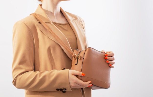 Mulher de casaco bege com bolsa de cor caramelo no fundo branco