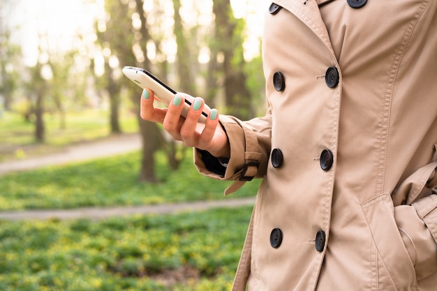 Mulher de casaco bege passeios no parque e usando um telefone celular