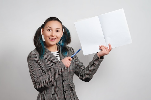 Mulher de casaco em um fundo claro. segurando um notebook com um espaço de cópia e mostra a caneta.