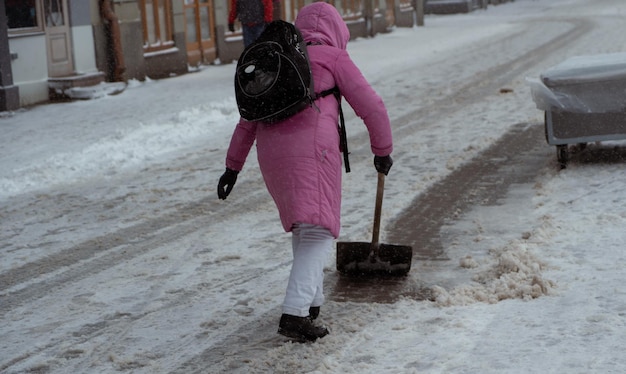 Mulher de casaco rosa e mochila preta limpando neve com pá na cidade