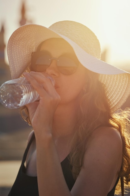 Foto mulher de chapéu bebendo água de garrafa no pôr do sol da noite de verão