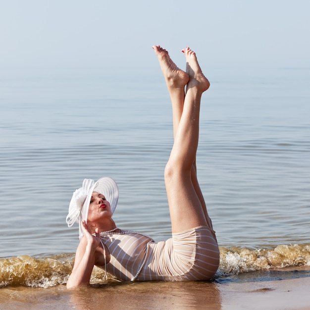 Mulher de chapéu branco posando contra o mar