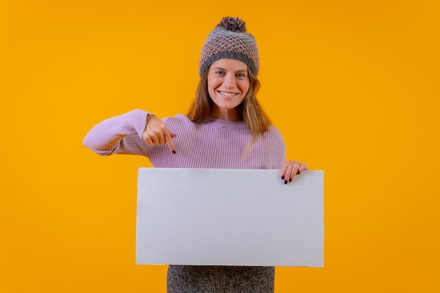 Mulher de chapéu de lã apontando para uma placa em um conceito de negócio de fundo amarelo