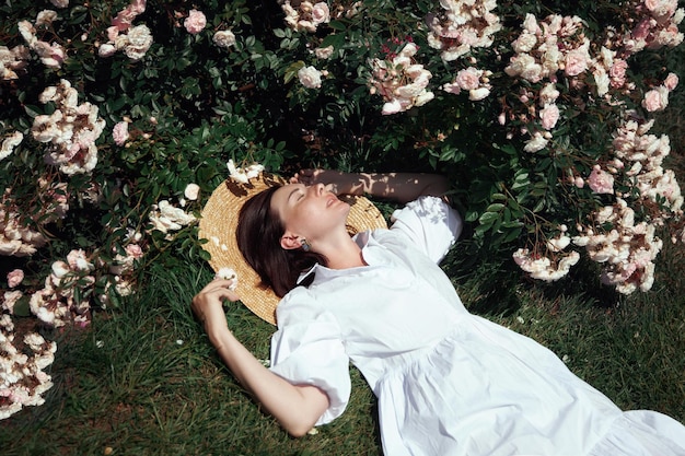 Mulher de chapéu e vestido branco no jardim contra o fundo de arbustos rosa Linda garota romântica