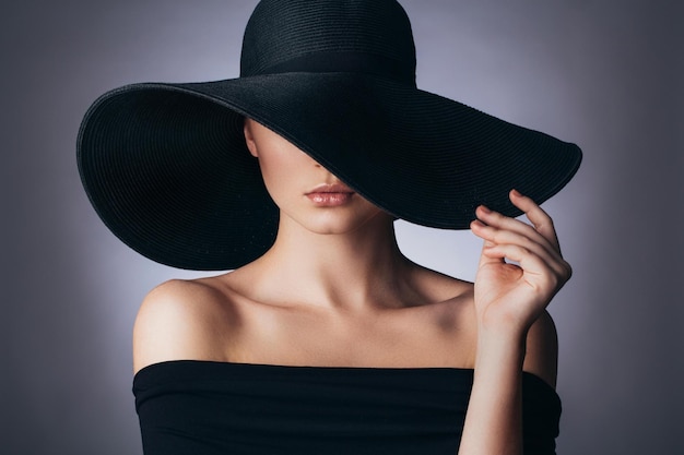 Mulher de chapéu preto com lábios vermelhos em fundo cinza foco seletivo Elegância e sensualidade feminina