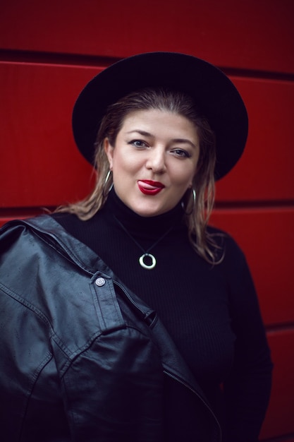 Mulher de chapéu preto e jaqueta de couro na parede vermelha