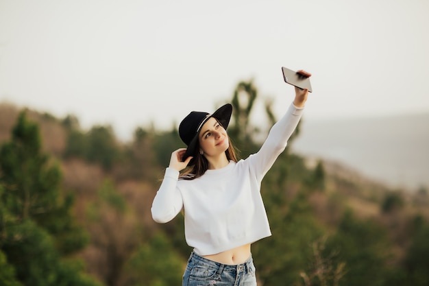 mulher de chapéu preto, fazendo selfie na floresta de montanha.