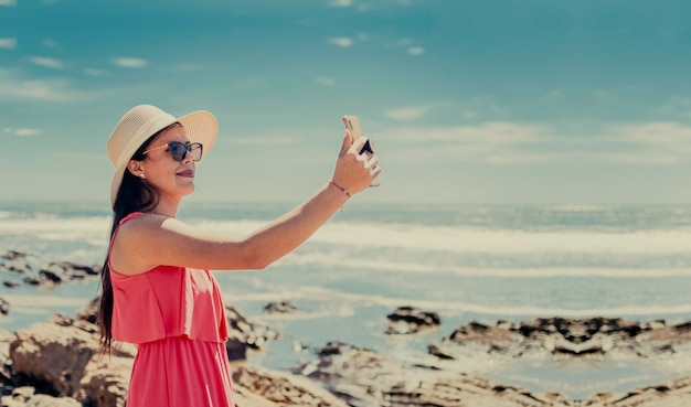 mulher de chapéu tirando fotos no mar garota tirando fotos de férias garota tirando selfie na praia