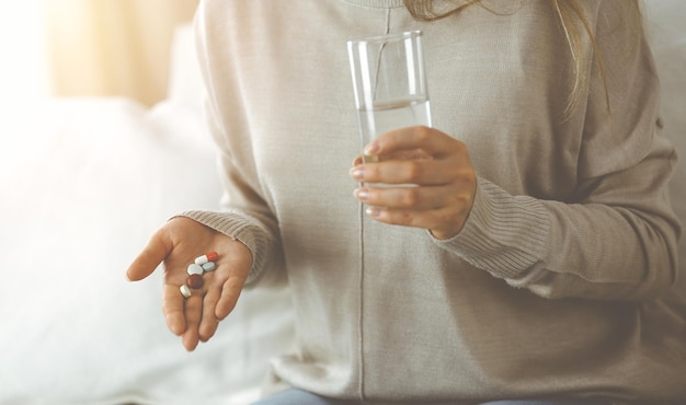 Mulher de close-up segurando comprimidos tempo para tomar medicamentos, cura para dor de cabeça. Conceito de medicina durante o auto-isolamento e a pandemia de Coronavirus.