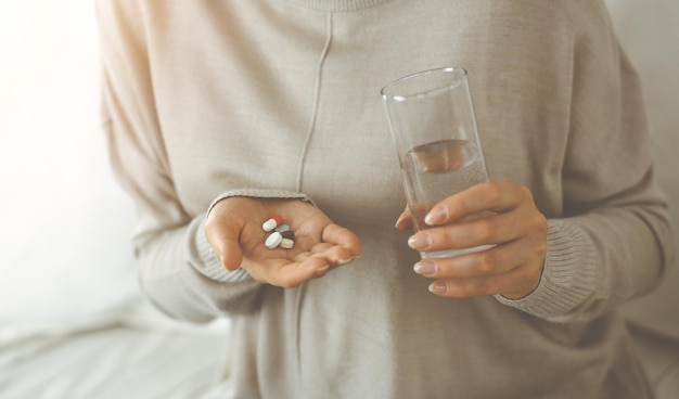 Mulher de close-up segurando pílulas na hora de tomar medicamentos, cura para dor de cabeça. Conceito de medicina durante o auto-isolamento e a pandemia de Coronavirus.