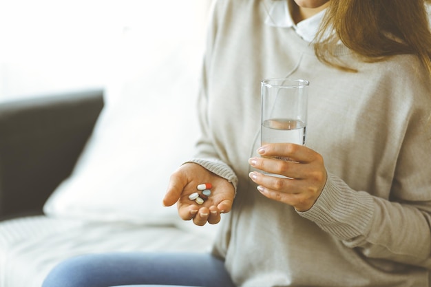 Mulher de close-up segurando pílulas na hora de tomar medicamentos, cura para dor de cabeça, medicamentos analgésicos para pressão alta em casa. Fique em casa conceito durante a pandemia de Coronavirus.