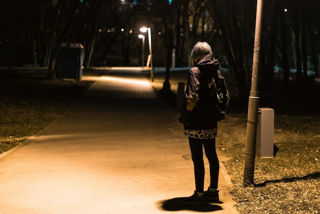 Foto mulher de comprimento completo com mochila de pé na calçada à noite