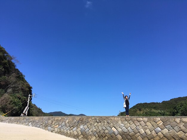 Foto mulher de comprimento completo com os braços levantados de pé na parede contra o céu azul