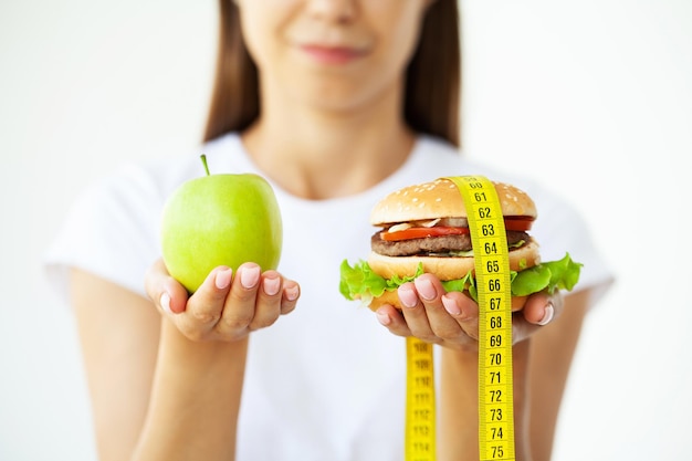 Mulher de conceito de dieta segurando uma escolha de hambúrguer prejudicial e maçã fresca