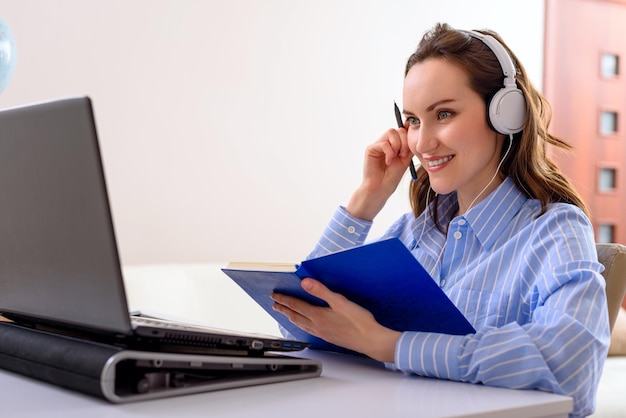 Mulher de conceito de educação online de camisa azul com fones de ouvido e notebook nas mãos sentada no laptop