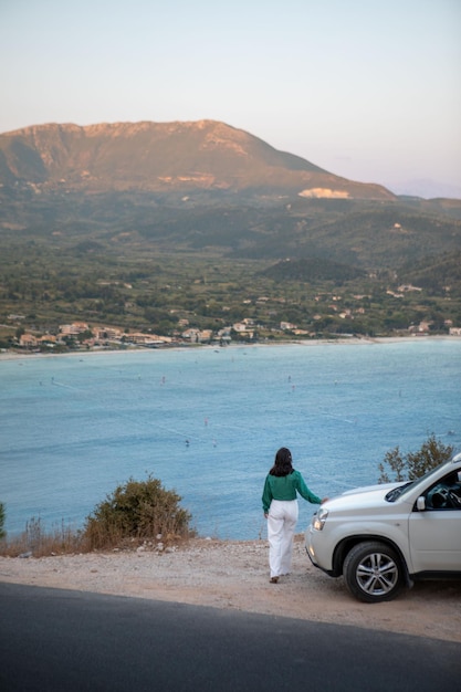 Mulher de conceito de viagem de carro em pé no penhasco olhando para a baía do mar