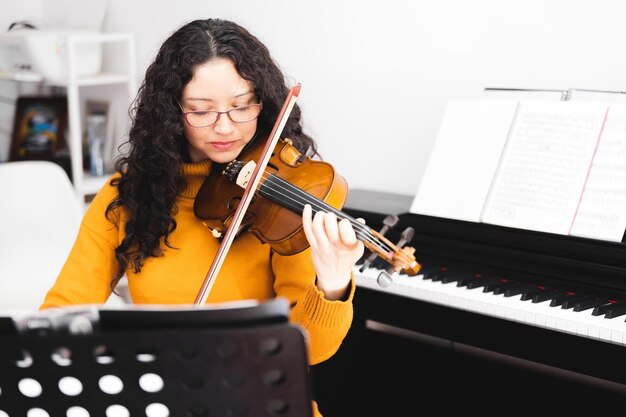 Mulher de concerto morena de olhos fechados vestindo suéter amarelo e tocando violino lendo partituras