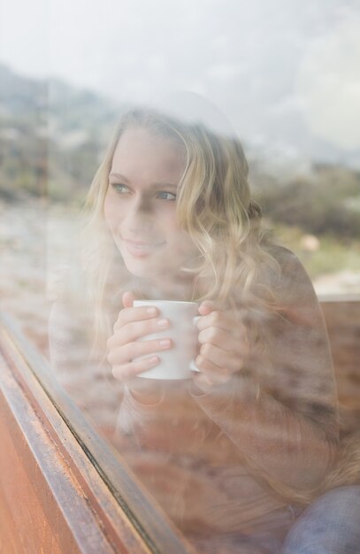 Mulher de conteúdo pensativo com copo de café olhando pela janela