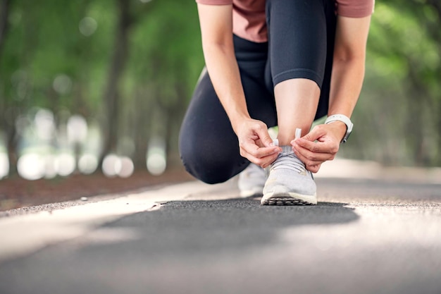 Mulher de corredor de sapatos de corrida amarrando cadarços para corrida de verão no parque florestal