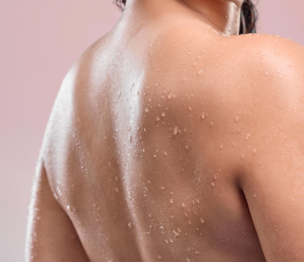 Mulher de costas e banho com água para alívio de estresse de higiene ou lavar em um fundo de estúdio rosa Vista traseira pessoa feminina ou modelo com líquido natural ou gotas em hidratação ou limpeza de cuidados com a pele