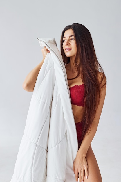 Mulher de cueca vermelha, cobrindo o corpo com uma toalha no estúdio contra um fundo branco.