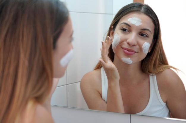 Mulher de cuidados com a pele aplicando creme na pele Tratamentos nutritivos e revigorantes para o rosto Aproveitando o tempo relaxante em casa