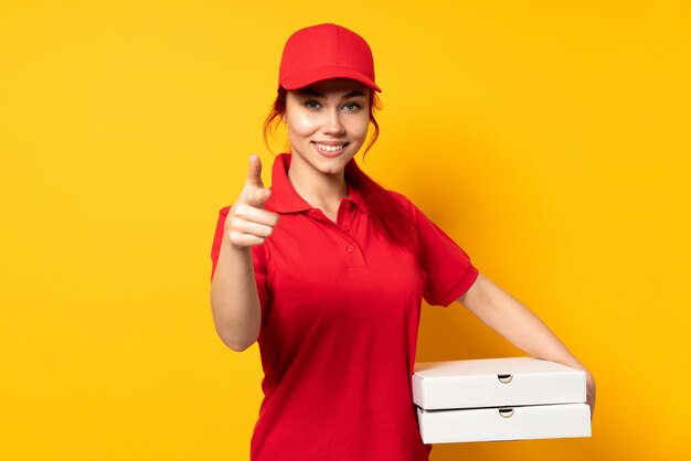 Mulher de entrega de pizza segurando uma pizza sobre parede isolada, apontando para a frente e sorrindo
