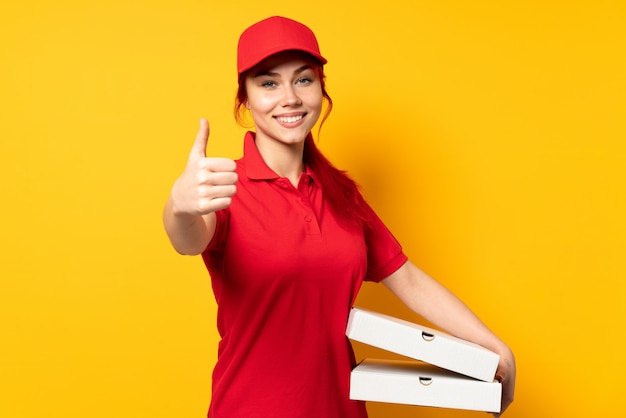 Mulher de entrega de pizza segurando uma pizza sobre parede isolada com polegares para cima, porque algo de bom aconteceu