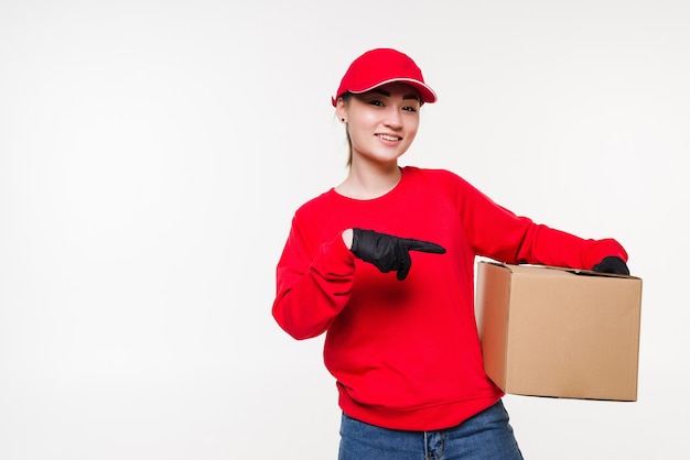 Mulher de entrega de uniforme vermelho isolado. Correio em luvas médicas, boné, camiseta vermelha trabalhando como negociante segurando uma caixa de papelão para entregar. Recebendo pacote.