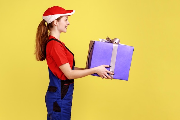 Mulher de entrega positiva em pé segurando a caixa de presente entregando presentes para feriados