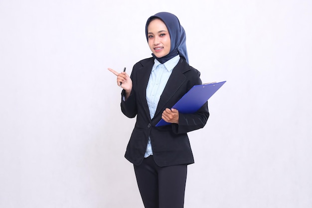 Mulher de escritório asiática vestindo um hijab de pé sorrindo alegremente apontando para a câmera carregando