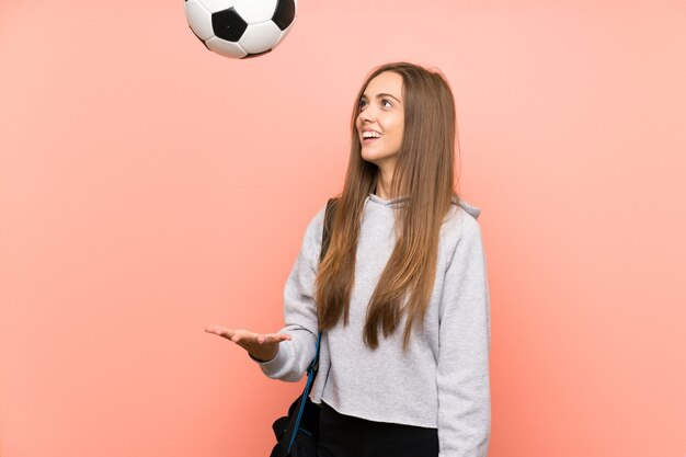 Mulher de esporte jovem feliz sobre fundo rosa isolado, segurando uma bola de futebol