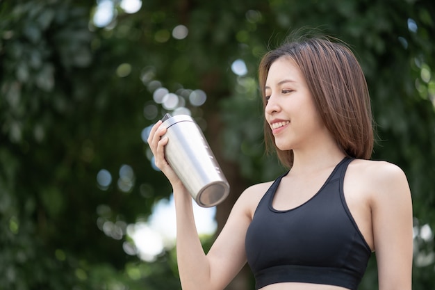 Mulher de esportes bebe shake de proteína do agitador de garrafa do liquidificador de aço inoxidável sobre fundo verde natural.