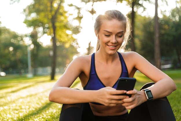 Mulher de esportes no parque ao ar livre, ouvindo música com fones de ouvido, usando telefone celular.