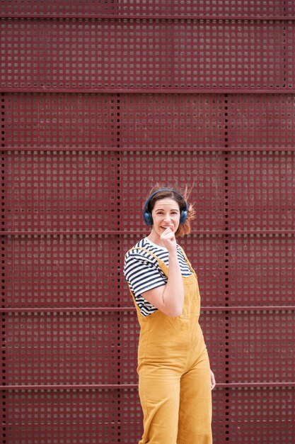 Mulher de estilo de vida com macacão amarelo cantando em um fundo vermelho Conceito liberdade divertida ao ar livre