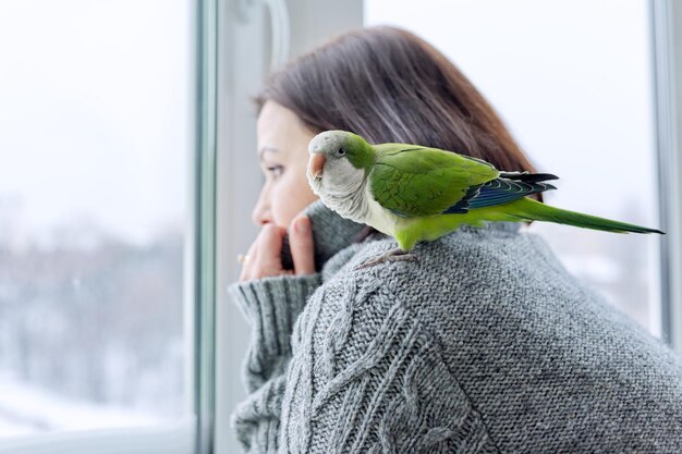 Foto mulher de estilo de vida em casa de inverno e papagaio olhando juntos pela janela de neve