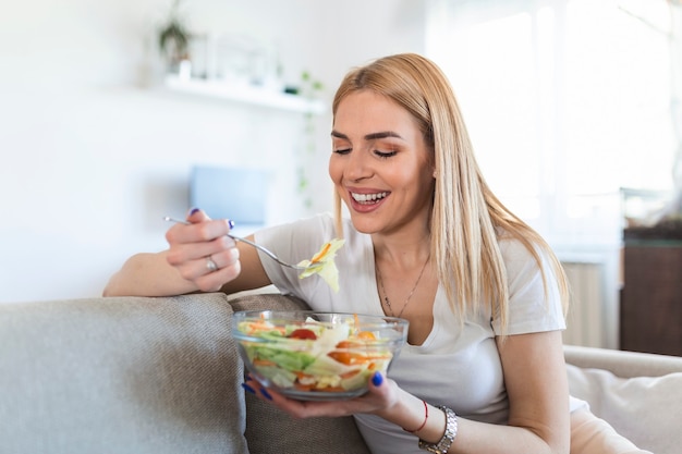 Mulher de estilo de vida saudável comendo salada, sorrindo feliz ao ar livre em um lindo dia. Jovem fêmea comendo alimentos saudáveis, rindo e relaxando no sofá.