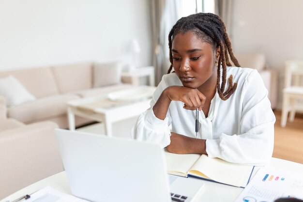 Mulher de etnia afro-americana sentada na mesa do local de trabalho olhando para a tela do laptop lendo e-mail sentindo-se preocupada entediada desmotivada cansada problemas de empregado dificuldades com o aplicativo