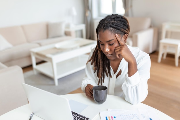 Mulher de etnia afro-americana sentada na mesa do local de trabalho olhando para a tela do laptop lendo e-mail sentindo-se preocupada entediada desmotivada cansada problemas de empregado dificuldades com o aplicativo