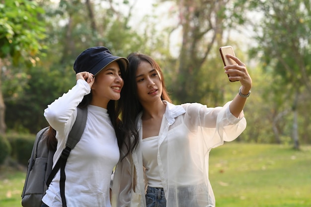 Mulher de faculdade asiática usando telefone inteligente, tomando selfie juntos no campus.