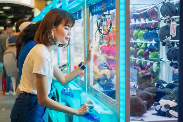 Mulher de felicidade jogando jogo de garra ou gabinete para pegar as bonecas