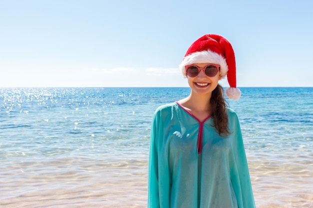 Mulher de férias com chapéu de Papai Noel relaxante na praia paradisíaca, férias de Natal