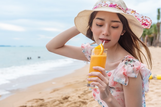 Mulher de férias de praia bebendo suco de laranja se divertindo na praia.