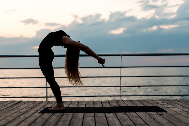 Foto mulher de fitness fazendo yoga e exercendo asana perto do mar no nascer do sol