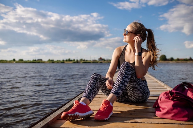 Mulher de fitness magro sentada e relaxada após treinamentos no cais no pôr do sol