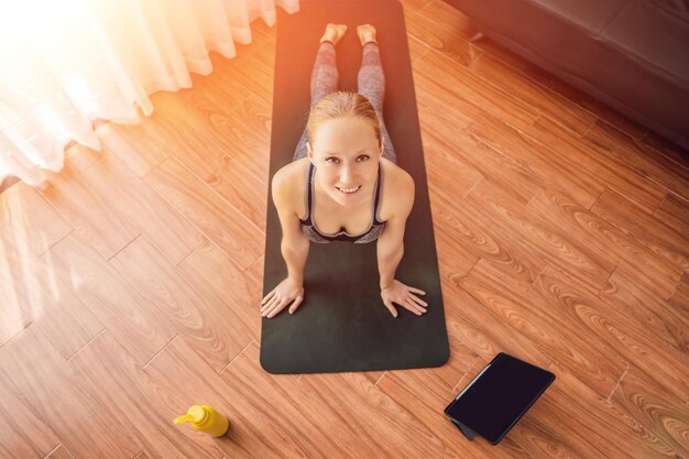 Mulher de fitness se exercitando no chão em casa e assistindo vídeos de fitness em um tablet que as pessoas fazem