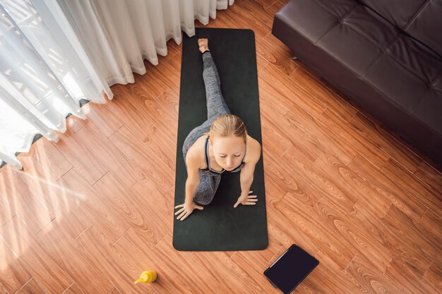 Mulher de fitness se exercitando no chão em casa e assistindo vídeos de fitness em um tablet que as pessoas fazem