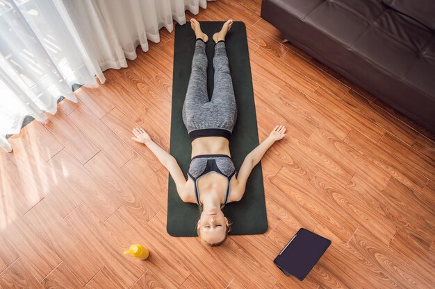 Mulher de fitness se exercitando no chão em casa e assistindo vídeos de fitness em um tablet que as pessoas fazem