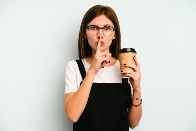 Mulher de garçom de restaurante segurando um café para viagem isolado em fundo azul, mantendo um segredo ou pedindo silêncio.