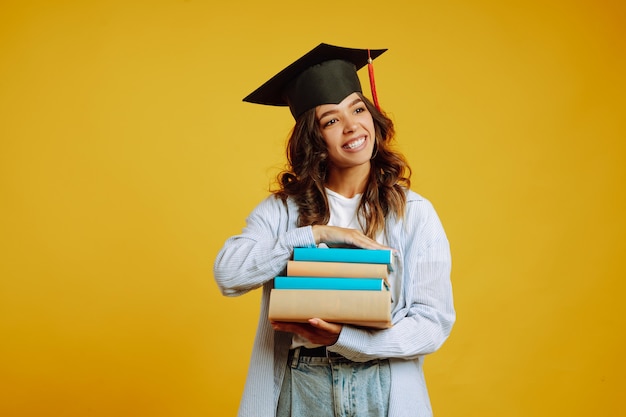 Mulher de graduação com um chapéu de formatura na cabeça, com livros em amarelo.